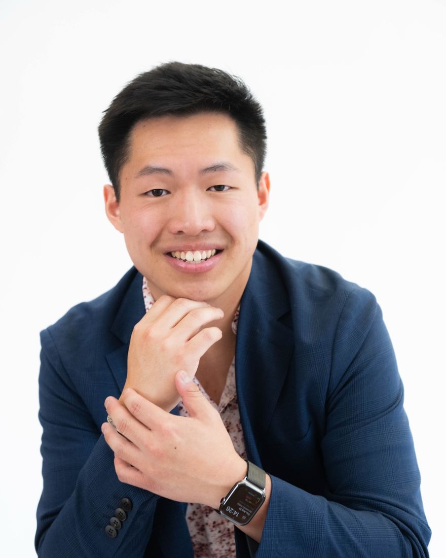 Phelim Jiang in a navy blazer, resting his chin on his hand and smiling